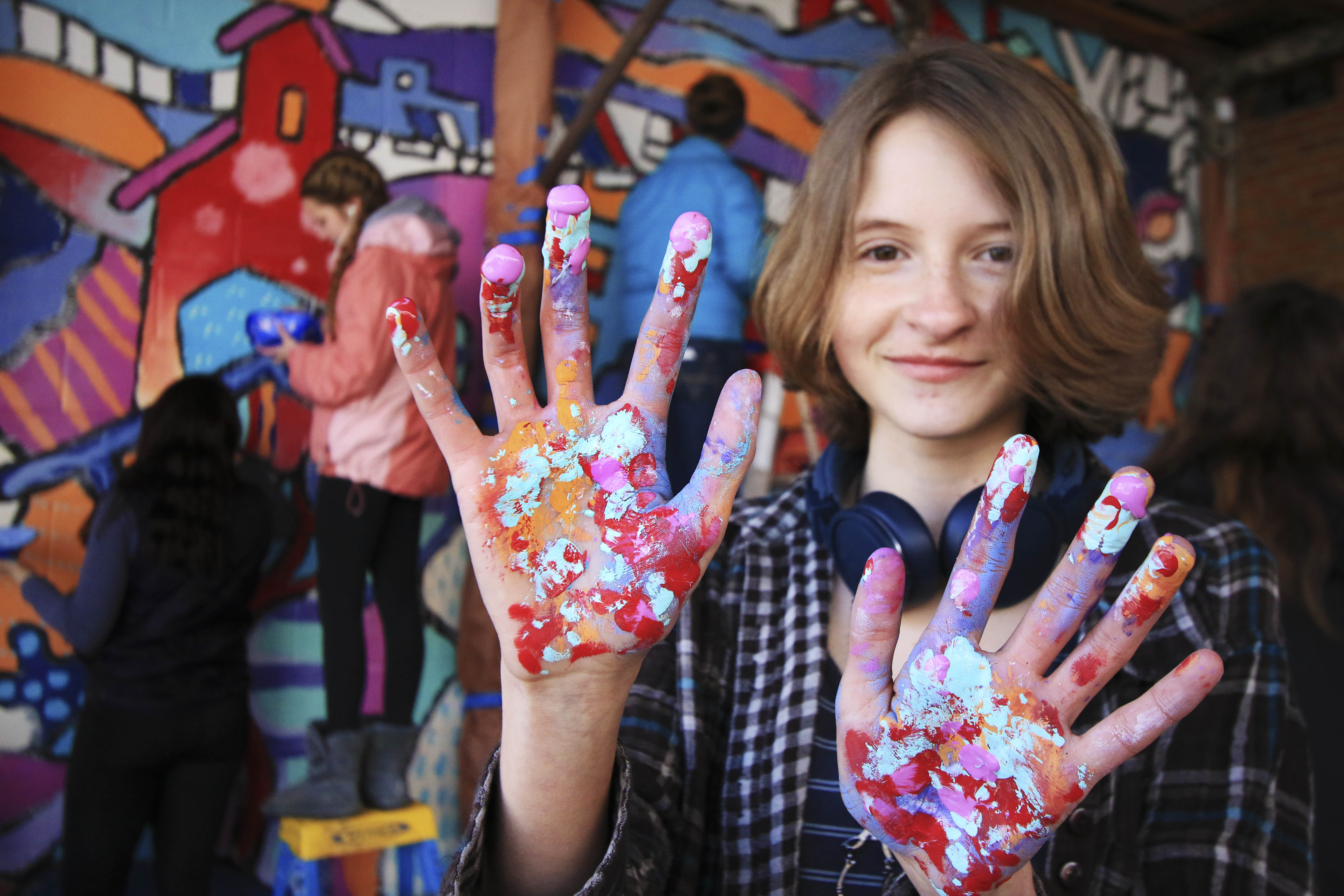 Sophia Cajune shows her messy hands as she and her Park High School classmates work on a mural project, guided by Tenesse artist Andee Rudloff, in an alley behind Out of the Blue Antiques in downtown Livingston on Tuesday afternoon.